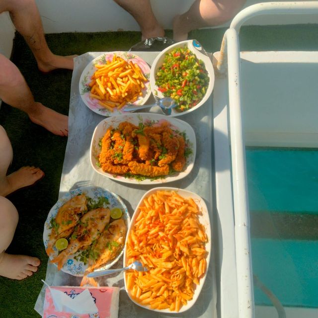 Boat lunch of grilled fish, fried strips, fries, pasta and salad beside a glass-bottom panel over turquoise water
