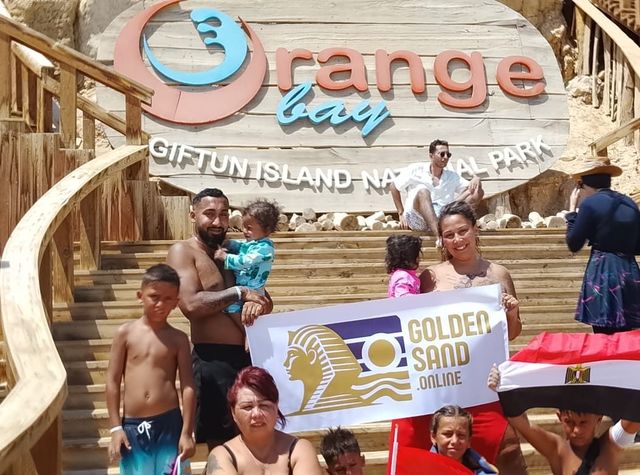 Hosté a děti s transparentem a egyptskou vlajkou pod nápisem Orange Bay na ostrově Giftun
