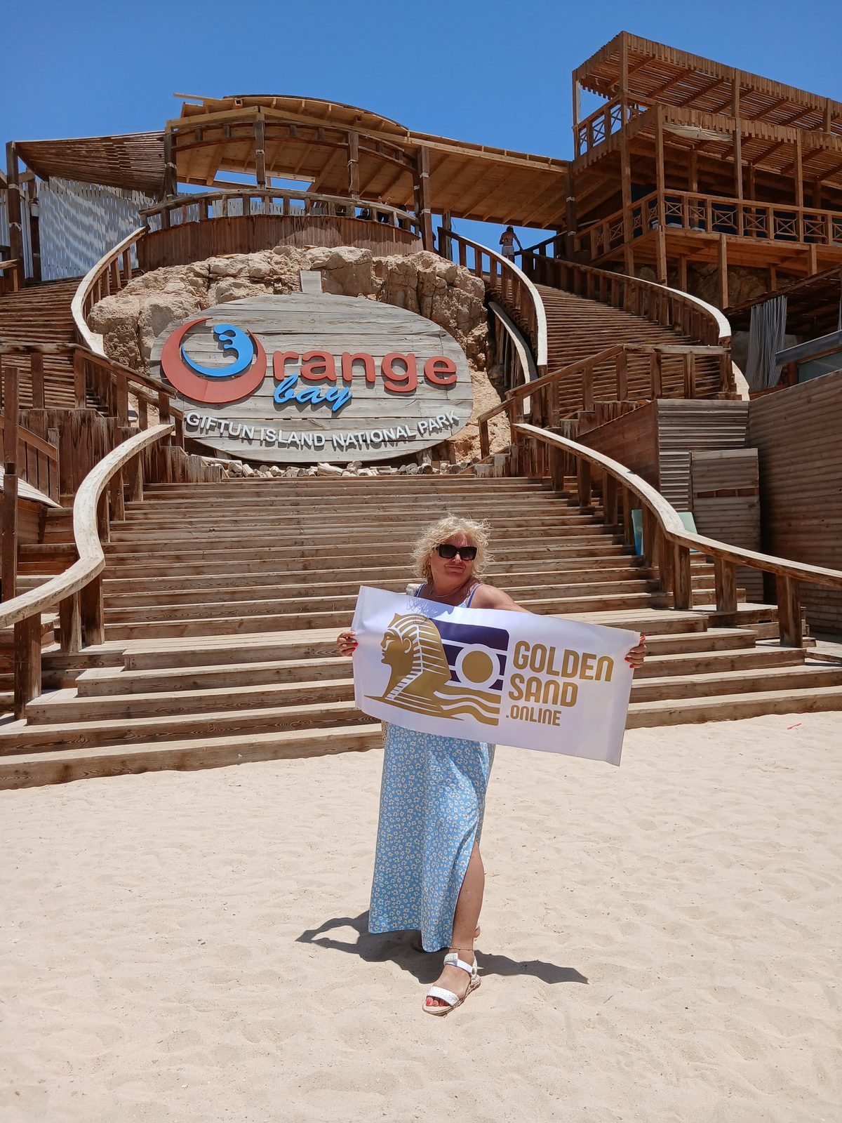 Golden Sand guest holding a banner on the beach below the Orange Bay sign at Giftun Island National Park