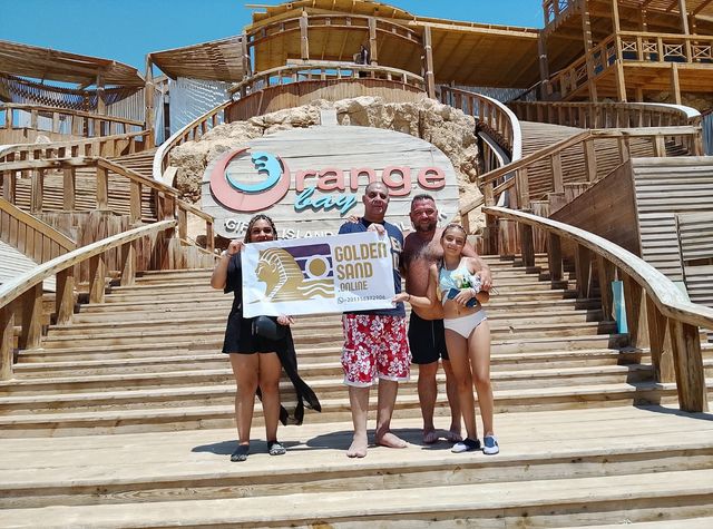 Golden Sand guests holding the company banner on the wooden steps beneath the Orange Bay sign on Giftun Island