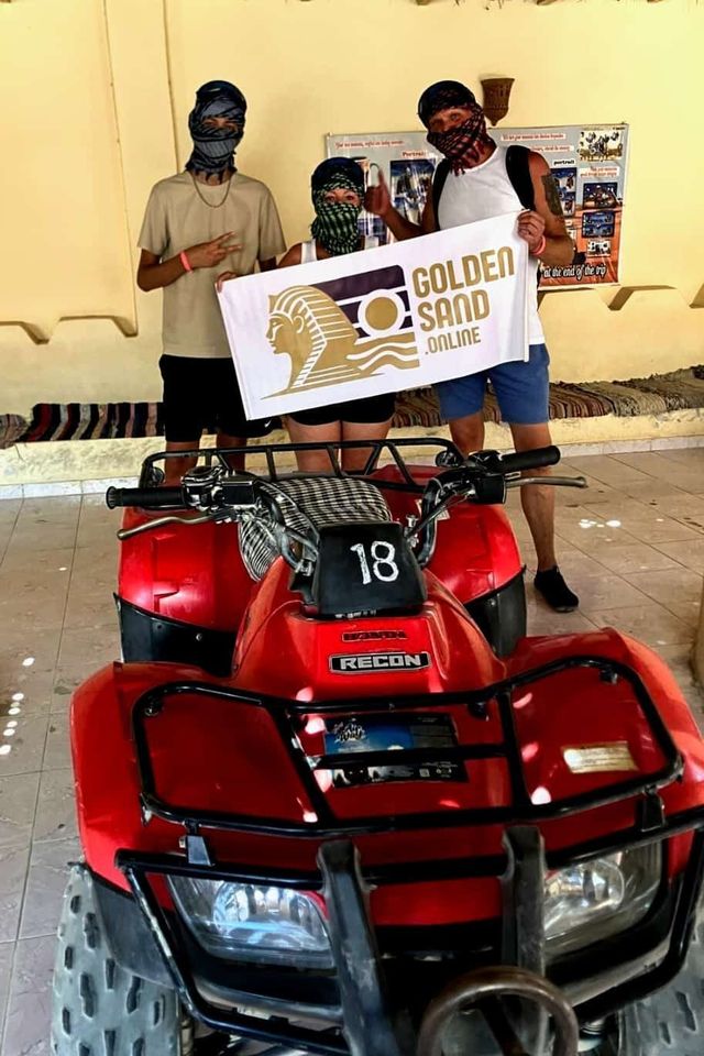 Tři hosté v pouštních šátcích drží transparent Golden Sand za červenou čtyřkolkou