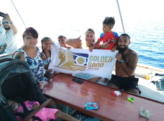 Golden Sand guests, including children, posing with a banner on a boat deck at sea