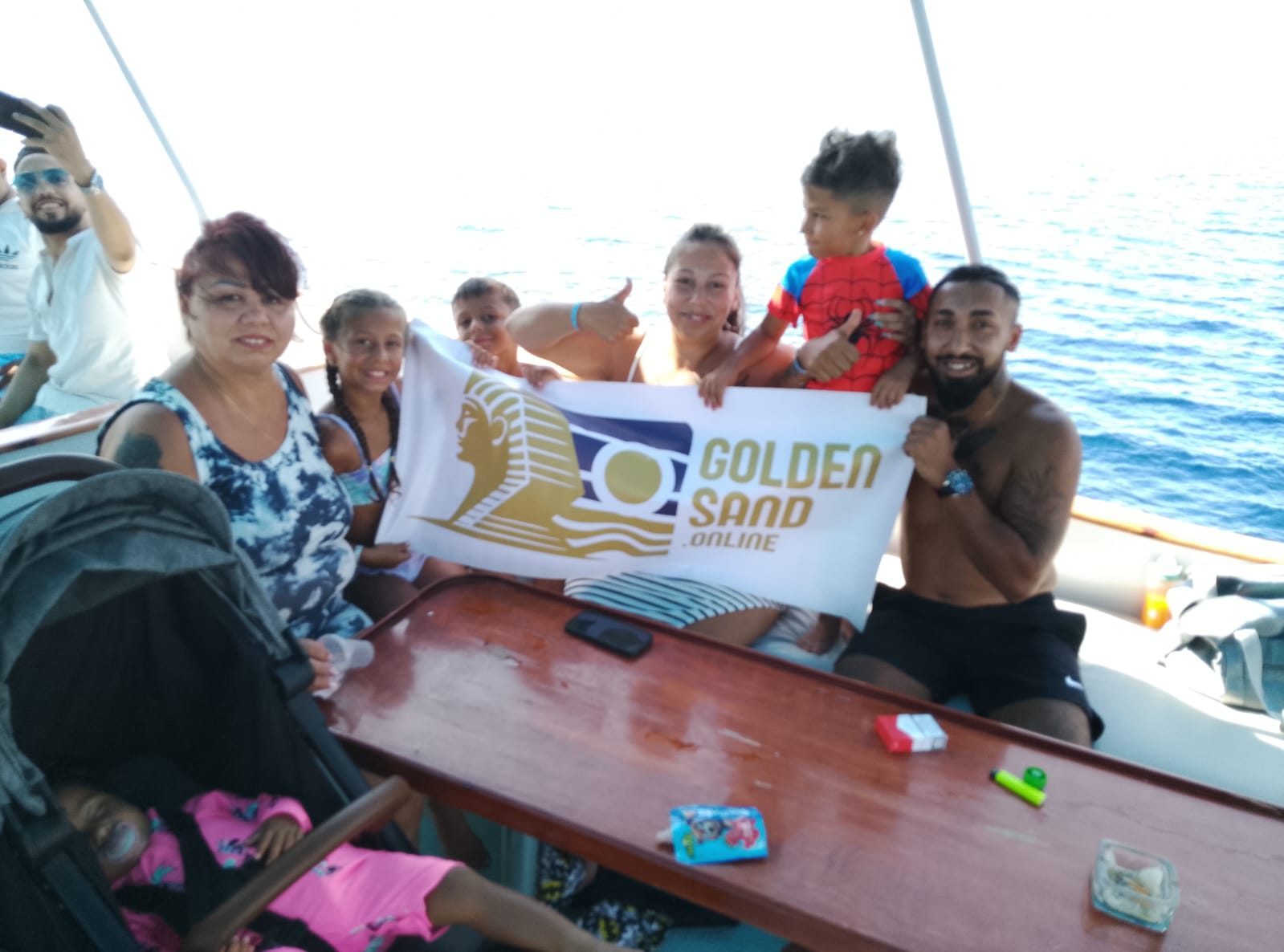 Golden Sand guests, including children, posing with a banner on a boat deck at sea