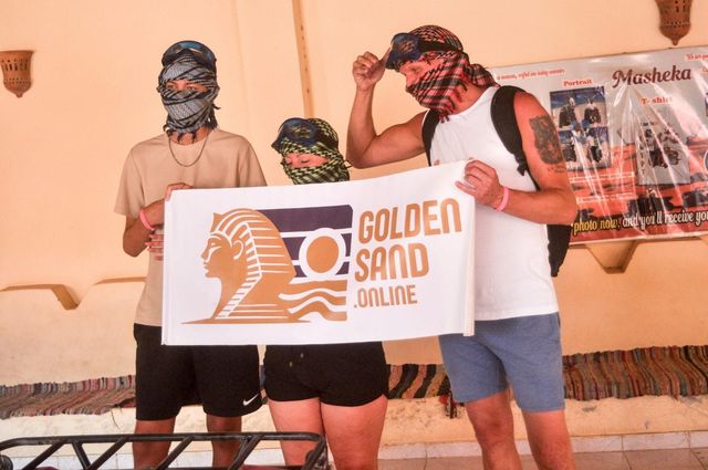 Tři hosté v šátcích drží velký transparent Golden Sand během zastávky na safari