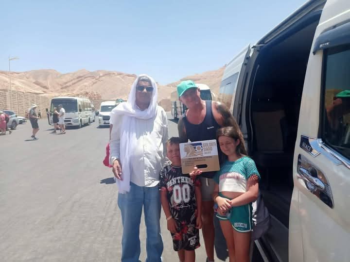 ضيوف فندق «Golden Sand» يلتقطون صورة مع لافتة الشركة بجانب حافلة صغيرة أمام تلال الصحراء
