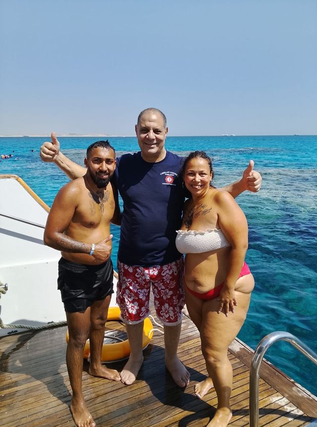 Three guests posing with thumbs up on a wooden boat deck beside a swim ladder over the Red Sea
