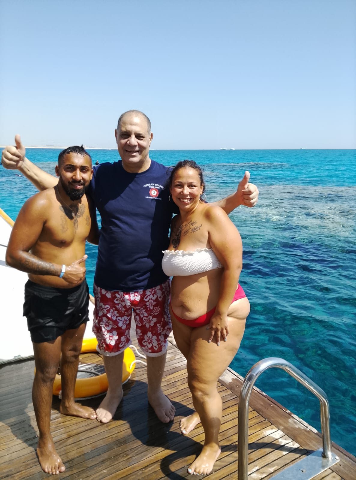 Golden Sand guests giving thumbs up on a boat deck above turquoise coral reef water in the Red Sea