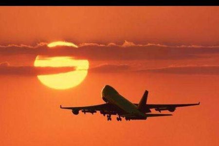 Passenger jet silhouetted against an orange sunset sky with the sun behind low clouds