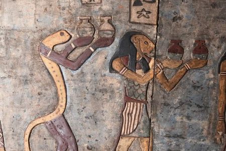 Close-up of a painted ancient Egyptian relief showing a snake-headed figure and an animal-headed figure carrying jars