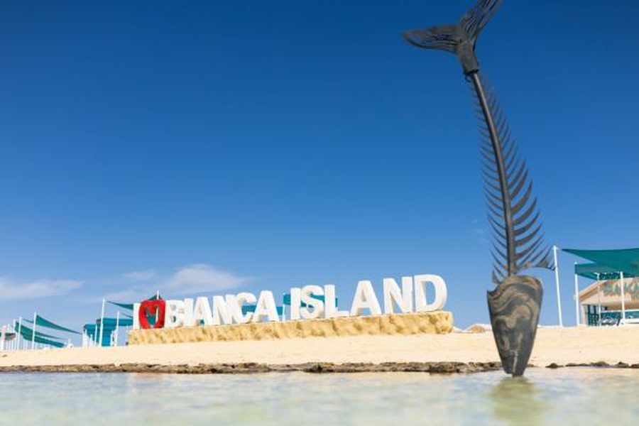 I Love Bianca Island sign on the beach with teal shade sails and a fish-skeleton sculpture in the shallows