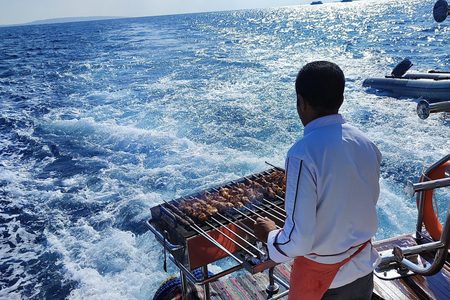 Crew member grilling meat skewers on the stern of a boat with foaming blue sea behind, on a trip from Hurghada