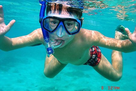 Boy with a blue mask and snorkel swimming underwater in clear turquoise water near Hurghada