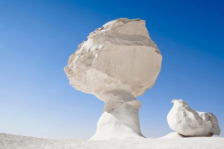 Mushroom-shaped chalk rock and a smaller chicken-shaped formation in the White Desert under a clear blue sky