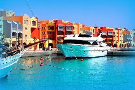 White motor yacht moored at a marina lined with colorful orange and red buildings in Hurghada