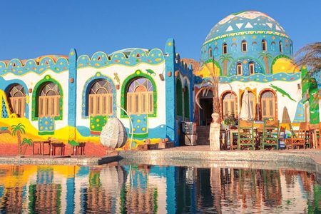 Brightly painted Nubian-style house with a blue dome and palm trees, reflected in a pool in Aswan