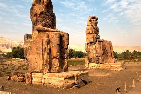The Colossi of Memnon, two giant weathered statues on Luxor's West Bank, with desert cliffs behind