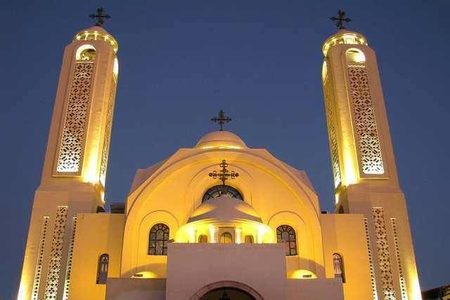 Coptic church with two floodlit towers and crosses glowing gold against the dark evening sky