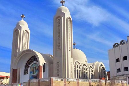 Coptic church with two tall towers and crosses under a deep blue sky with wispy clouds
