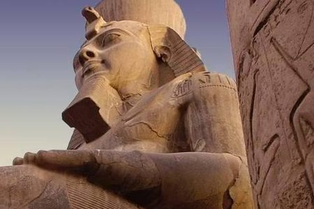 Crowned and bearded stone pharaoh statue towering beside a carved column at a temple in Luxor