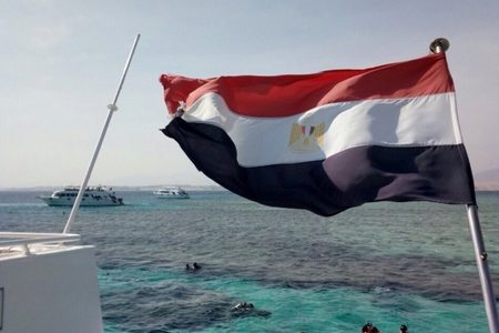 Egyptian flag flying on a boat with snorkelers in life jackets swimming in turquoise Red Sea water
