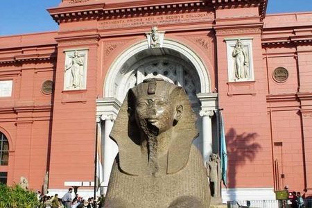 Rose-pink facade of the Egyptian Museum in Cairo with a stone sphinx statue in front of the entrance