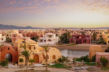 Terracotta and sand-colored domed houses beside a lagoon at sunset in El Gouna with palm trees