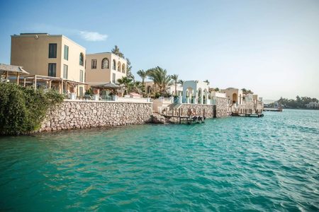 Sand-colored villas with arched terraces behind a stone sea wall and turquoise water in El Gouna