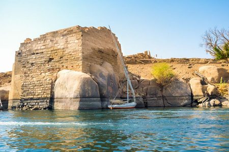 Felucca sailboat beside an ancient stone ruin and granite boulders on the bank of the Nile