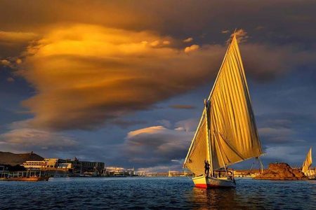 Traditional felucca sailboat on the Nile at sunset under dramatic golden clouds