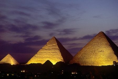 Illuminated Giza pyramids glowing gold at dusk under a purple, cloudy sky