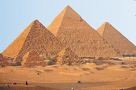 The Giza pyramids rising above desert sand in warm golden sunlight under a pale blue sky