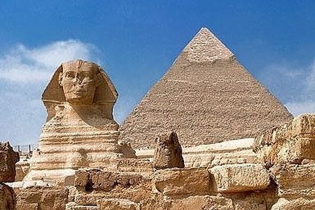 Rostro de la esfinge junto a una gran pirámide, con bloques de piedra caliza desgastados por la intemperie en primer plano