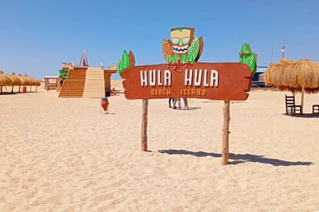 Hula Hula Beach Island sign on a white sand beach with thatched sunshades and wooden steps near Hurghada