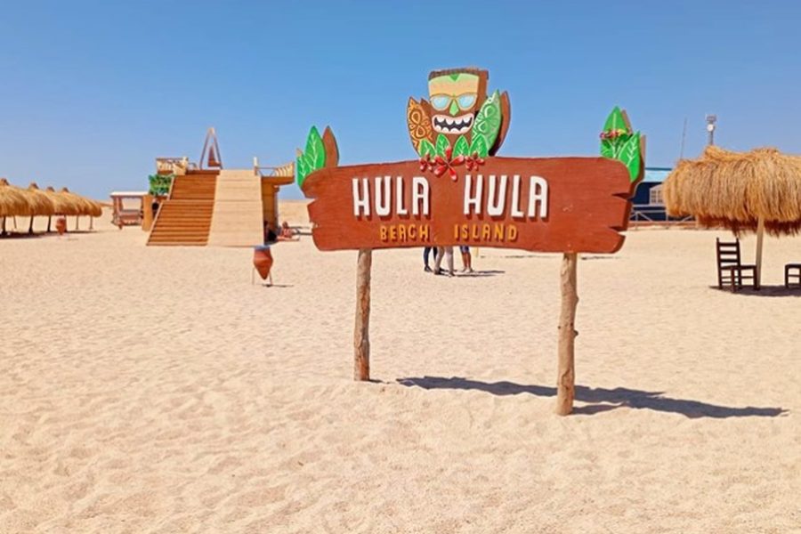 Hula Hula Beach Island sign on a white sand beach with thatched sunshades and wooden steps near Hurghada