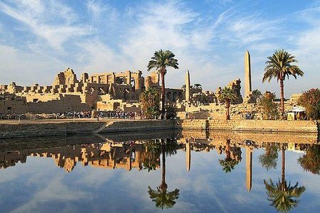 Sacred Lake at Karnak Temple reflecting an obelisk, palm trees and temple ruins under a blue sky in Luxor