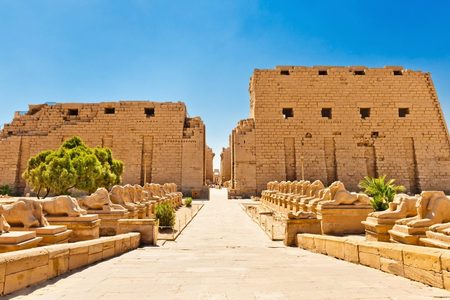 Rows of ram-headed sphinx statues lining the stone path to the great pylon gateway at Karnak Temple