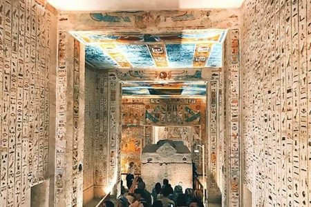 Visitors walk down a painted tomb corridor with hieroglyphs toward a sarcophagus in the Valley of the Kings