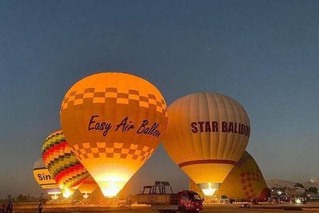 Glowing hot air balloons being inflated at twilight on a launch field in Luxor