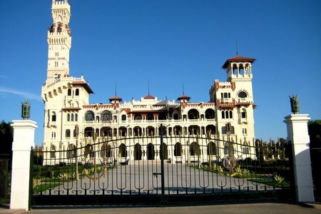 Montaza Palace with its tall tower and red-tiled turrets seen through an ornate iron gate in Alexandria