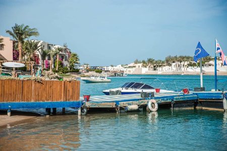 Motorboats moored at a wooden jetty on a turquoise lagoon with palm trees and white villas in El Gouna