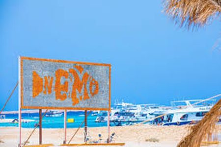 Weathered wooden beach sign with tourist boats moored in the bay at Nemo Bay Island