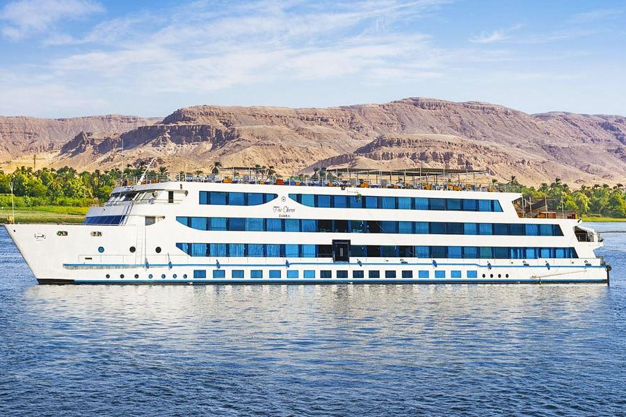 White multi-deck Nile cruise ship sailing past palm trees and brown desert hills