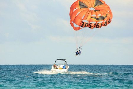 Two parasailers in blue life vests under an orange parachute towed behind a white speedboat at sea