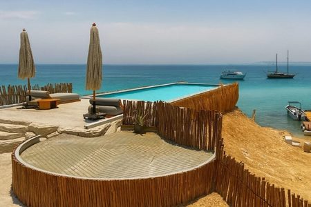 Seaside terrace with a turquoise pool, straw umbrellas and a small jetty with boats on Ozirea Island