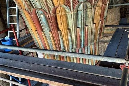 Painted palm-frond column capital in an ancient Egyptian temple, partly hidden behind scaffolding planks