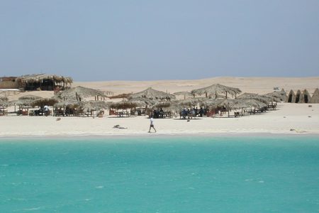 Thatched beach shelters on pale sand beside turquoise water, seen from a boat at Paradise Island near Hurghada