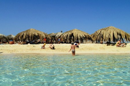 Tourists and children on the sandy beach of Paradise Island with palm-thatched shelters and clear shallow water