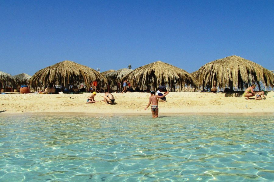 Tourists and children on the sandy beach of Paradise Island with palm-thatched shelters and clear shallow water
