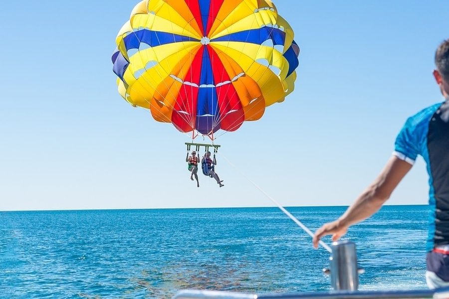 Deux touristes faisant du parachute ascensionnel sous un arc-en-ciel aux couleurs vives au-dessus de la mer, au large d'Hurghada ; un membre de l'équipage du bateau tient la corde
