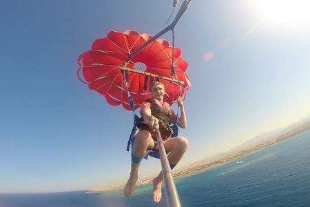سائحان يمارسان رياضة التزلج الهوائي تحت قوس قزح لامع فوق البحر قبالة الغردقة (Hurghada)، وأحد أفراد طاقم القارب يمسك بالحبل